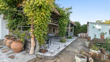 Un patio empedrado con plantas en macetas, un pérgola y un edificio rústico con techo de tejas.