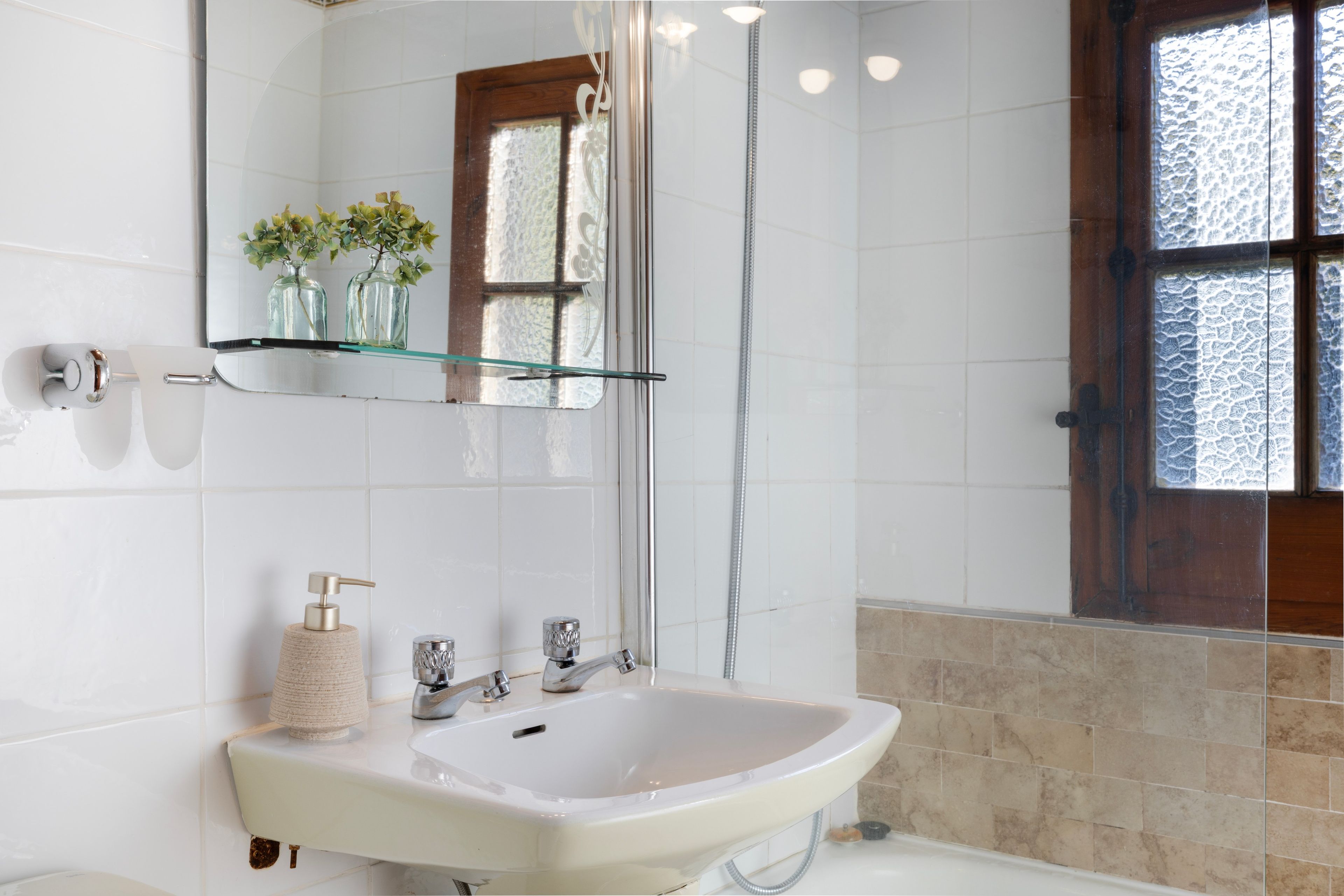 A bathroom with a white sink, a glass shelf with vases, and a shower area.
