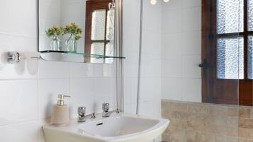 A bathroom with a white sink, a glass shelf with vases, and a shower area.