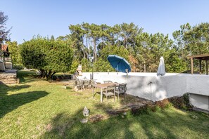 A patio area with a table and chairs, a blue umbrella, and a white wall.