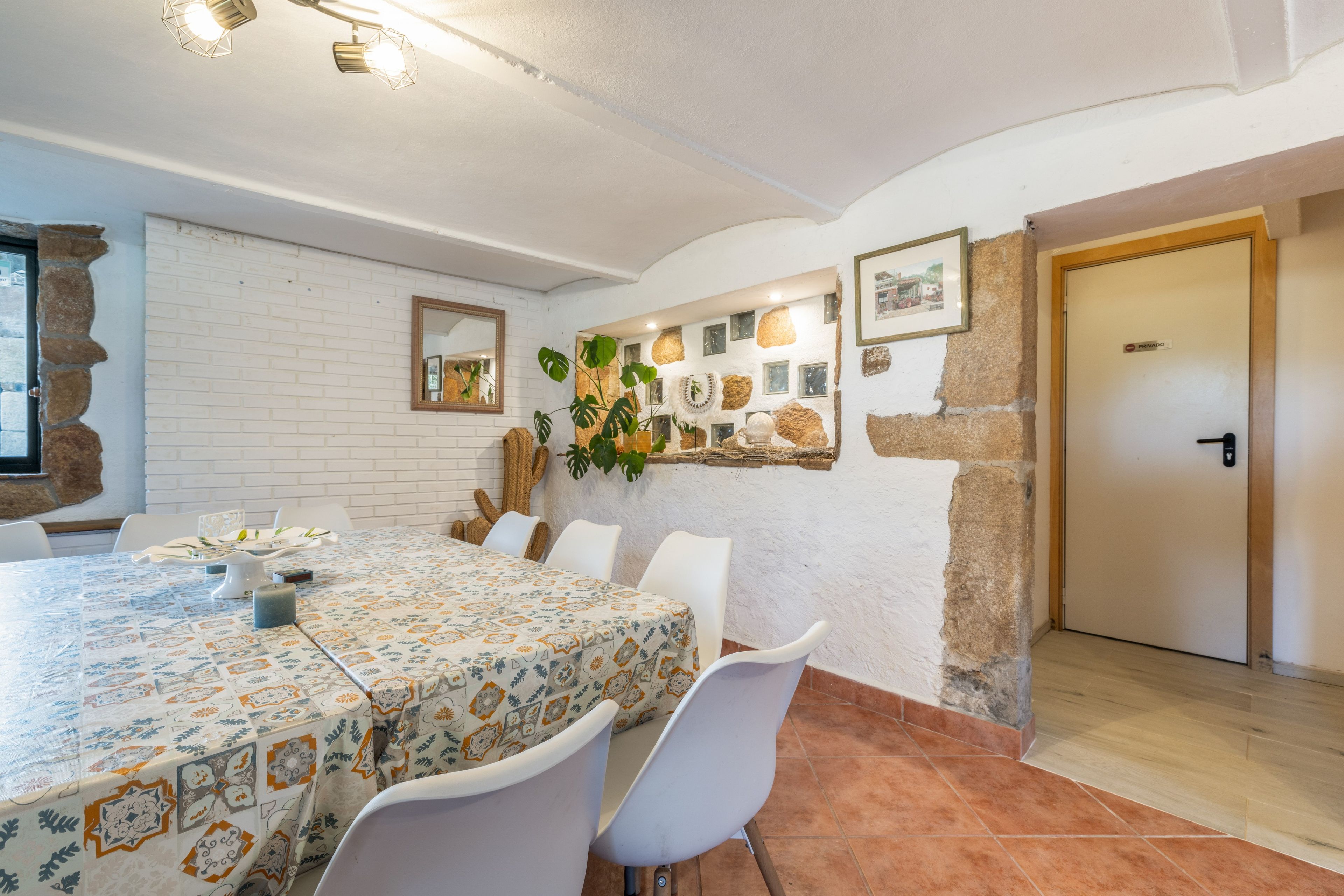 A dining area with a table set for four, white chairs, a patterned tablecloth, and a wall with a mix of brick and stone textures.