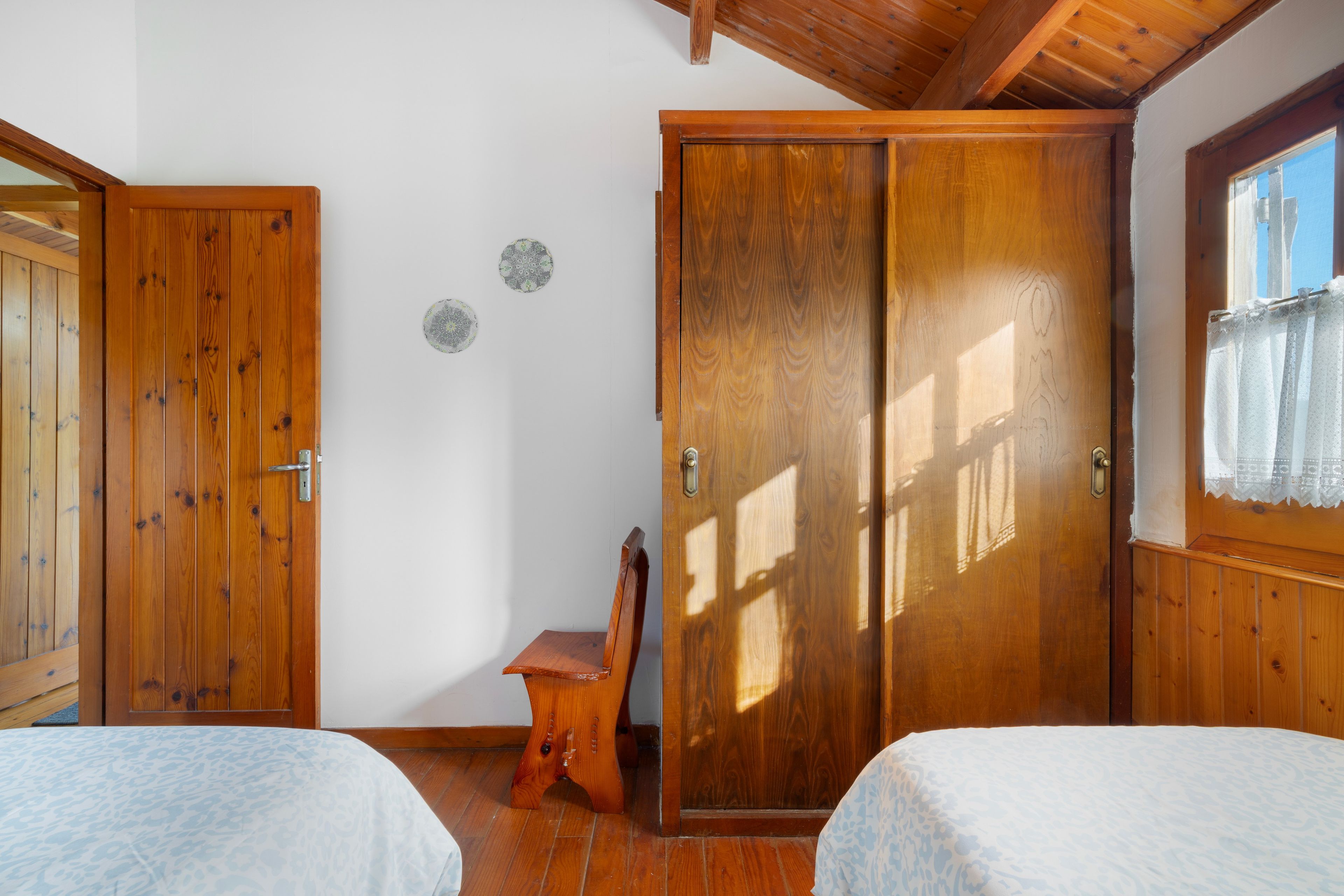 A bedroom with two wooden beds, a wooden wardrobe, and a small wooden chair.