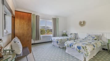 Una habitació amb dos llits, una porta de fusta, una finestra amb cortines, una taula de nit amb una làmpada i una decoració penjada a la paret.