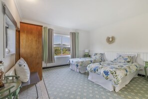 Et soveværelse med to senge, en trædør, et vindue med gardiner, et sengebord med en lampe og en dekoration på væggen.