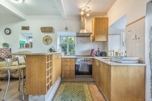 A compact kitchen with wooden cabinets, a built-in oven, and a window overlooking greenery. - Holiday Home 'Cottage' with Mountain View, Shared Pool and Wi-Fi (As Eiras)