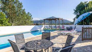 A poolside area with a pergola, lounge chairs, and a table.
