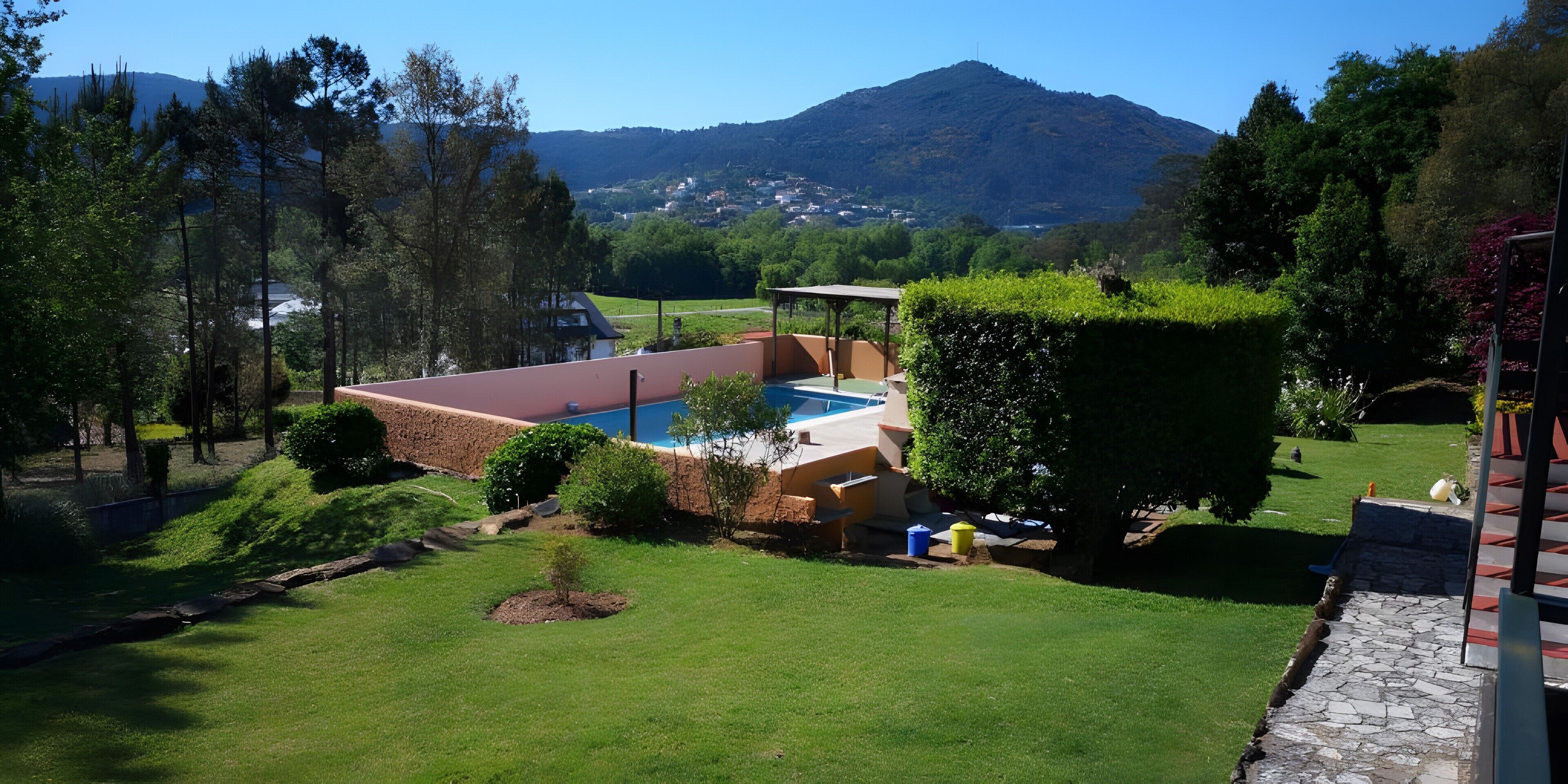 A pool with a red roof, surrounded by a well-maintained lawn and a mountain in the background.