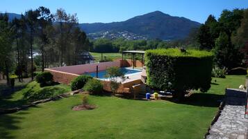 A pool with a red roof, surrounded by a well-maintained lawn and a mountain in the background.