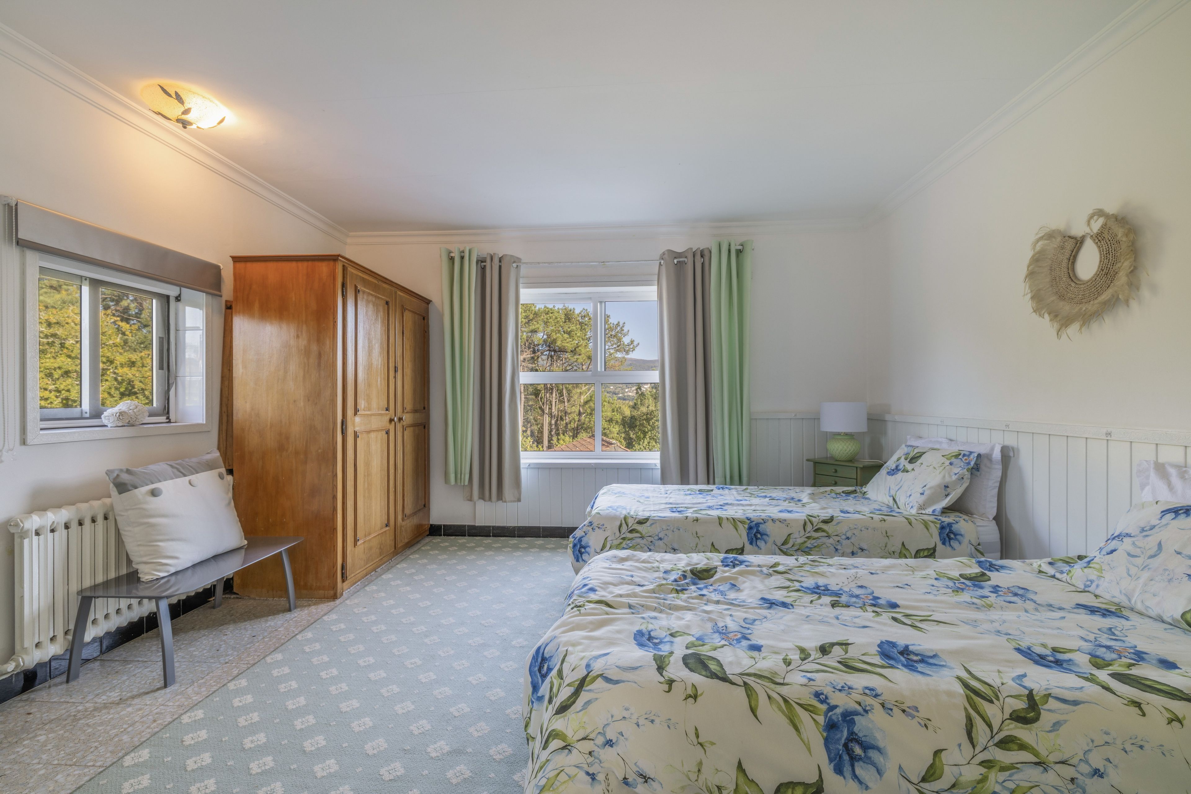 A bedroom with two beds, a wooden wardrobe, a radiator, and a window with curtains.