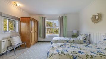 A bedroom with two beds, a wooden wardrobe, a radiator, and a window with curtains.