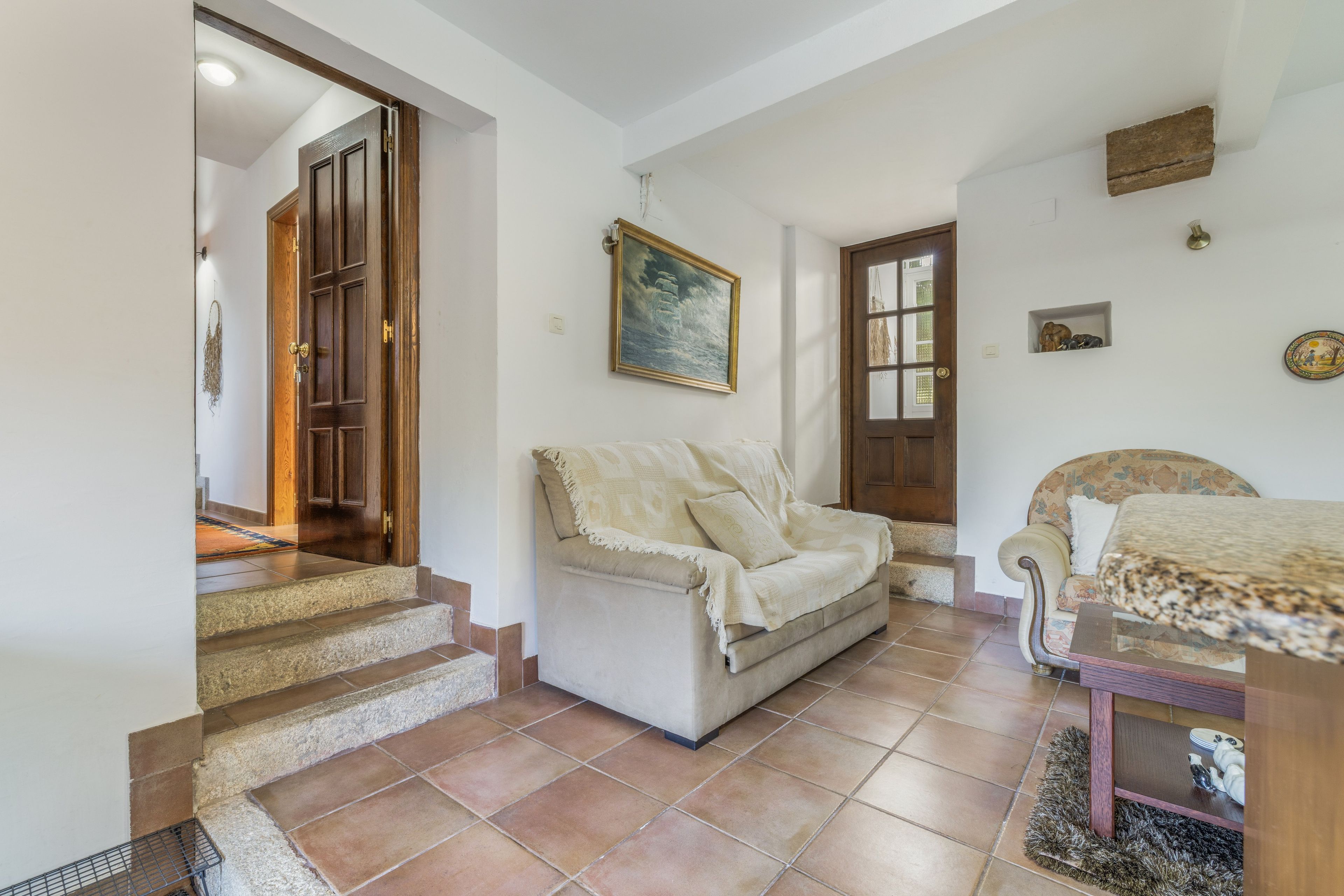 A room with a sofa, a dining table, a painting, and a staircase.