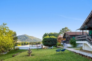 A well-maintained garden with a fountain, outdoor seating, and a view of a mountain.