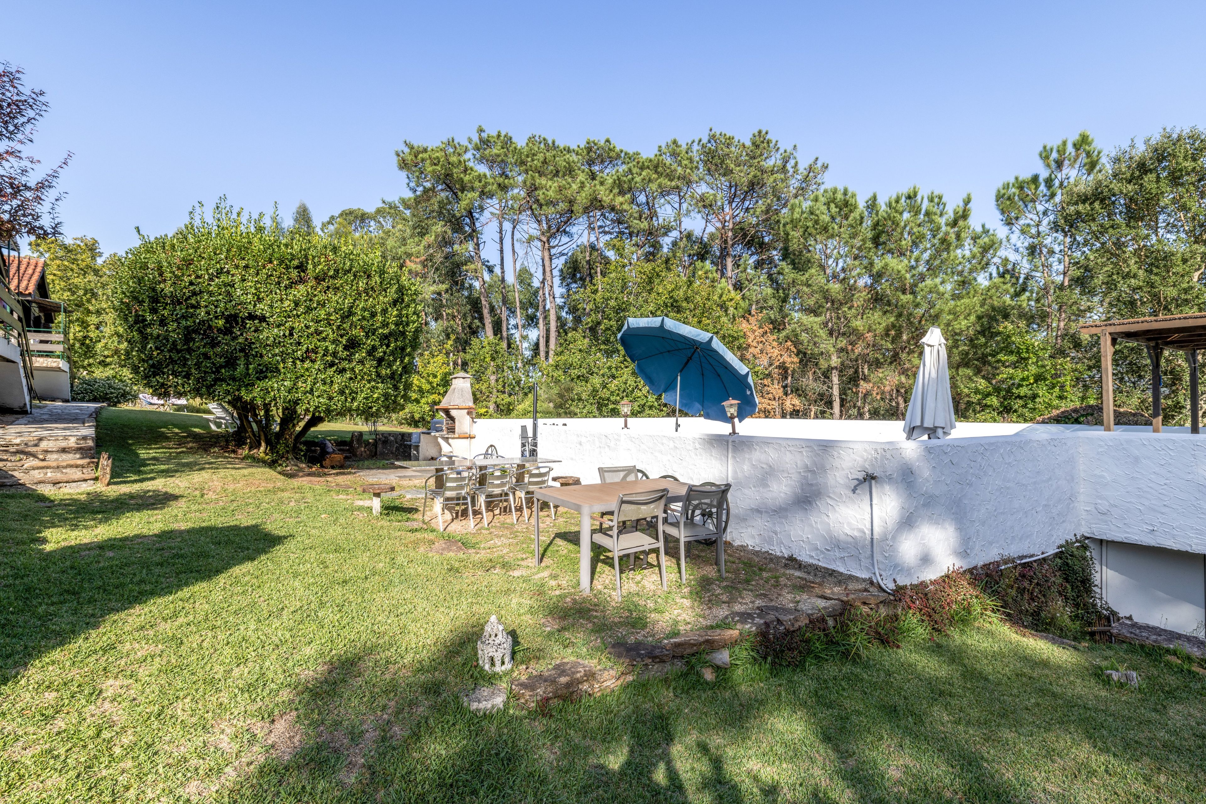 Eine Terrasse mit Tisch und Stühlen, umgeben von einer weißen Mauer und Bäumen.