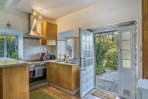 Una cocina con armarios de madera, estufa de acero inoxidable y ventana con vista a un jardín.