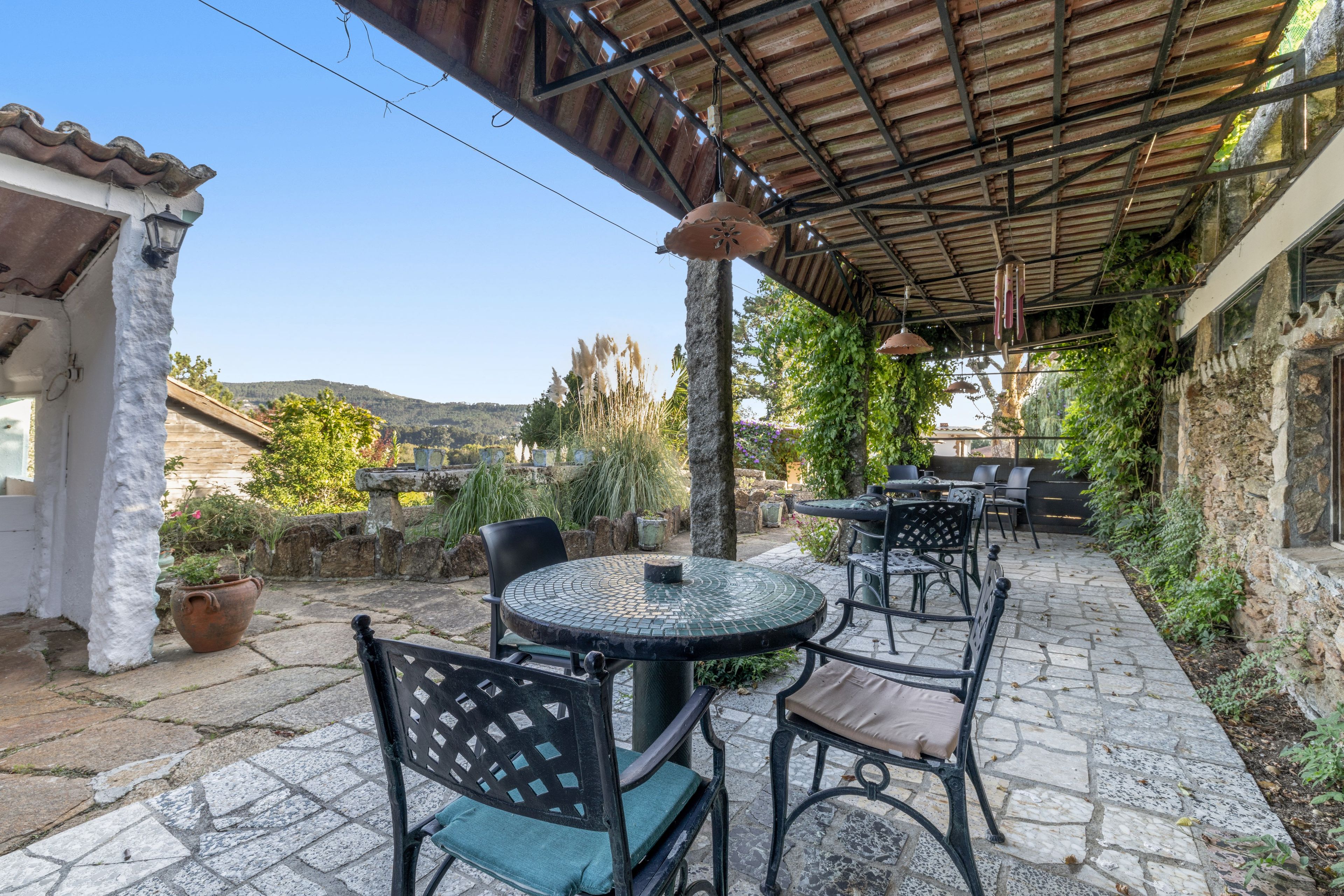 An outdoor patio area with stone flooring, metal tables and chairs, and a covered section with a metal roof.