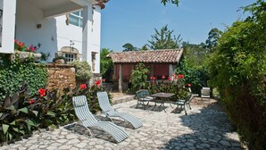 Un patio con dos sillones a rayas, una pequeña mesa y un camino de piedra que lleva a un edificio con tejado de baldosas.