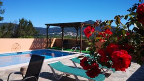 Un área de piscina con sillones de descanso, una pérgola y vistas al paisaje.