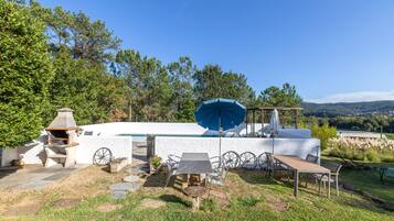 Eine Terrassenanlage mit Grill, Sitzgelegenheit und Blick auf Pool und Hügel.