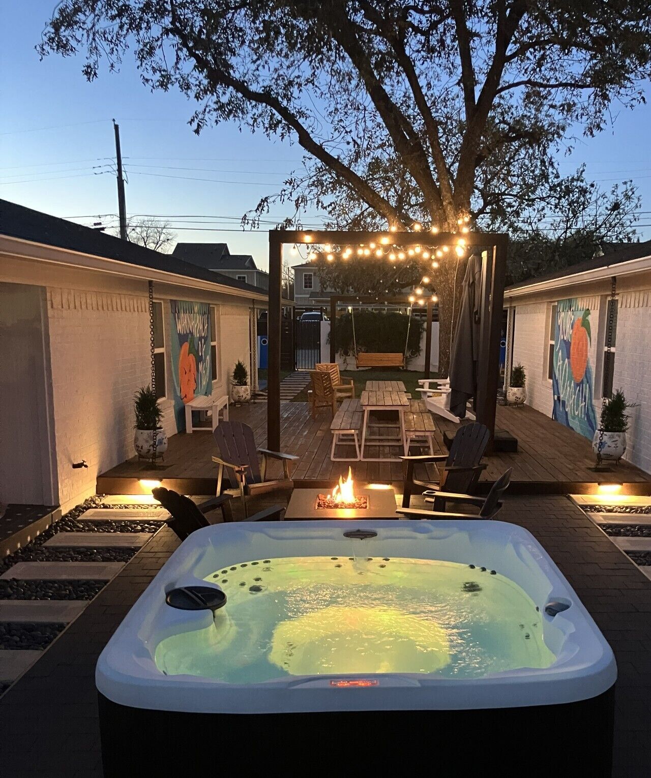 Un patio trasero con jacuzzi, mobiliario exterior e iluminación colgante.