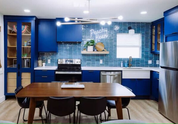 A modern kitchen with blue cabinets, a wooden dining table, and a stainless steel refrigerator.