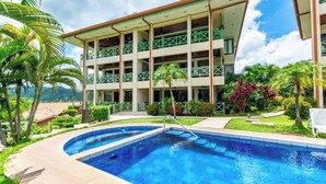 A hotel with a pool, multiple balconies, and lush greenery. - Elegant Condo with Brand-New Fixtures, Shaded Tropical Terrace, and Secluded Beach Access (Playa Flamingo)