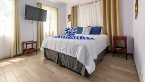 A bedroom with a bed, a TV, and two side tables. - Elegant Condo with Brand-New Fixtures, Shaded Tropical Terrace, and Secluded Beach Access (Playa Flamingo)