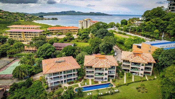 A resort with multiple buildings, a swimming pool, and a view of the sea. - Elegant Condo with Brand-New Fixtures, Shaded Tropical Terrace, and Secluded Beach Access (Playa Flamingo)