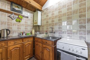 Une cuisine avec des meubles en bois, une cuisinière, un évier et un dosseret carrelé.