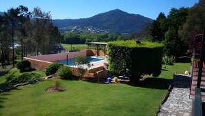 A pool with a red roof, surrounded by a well-maintained lawn and a mountain in the background.