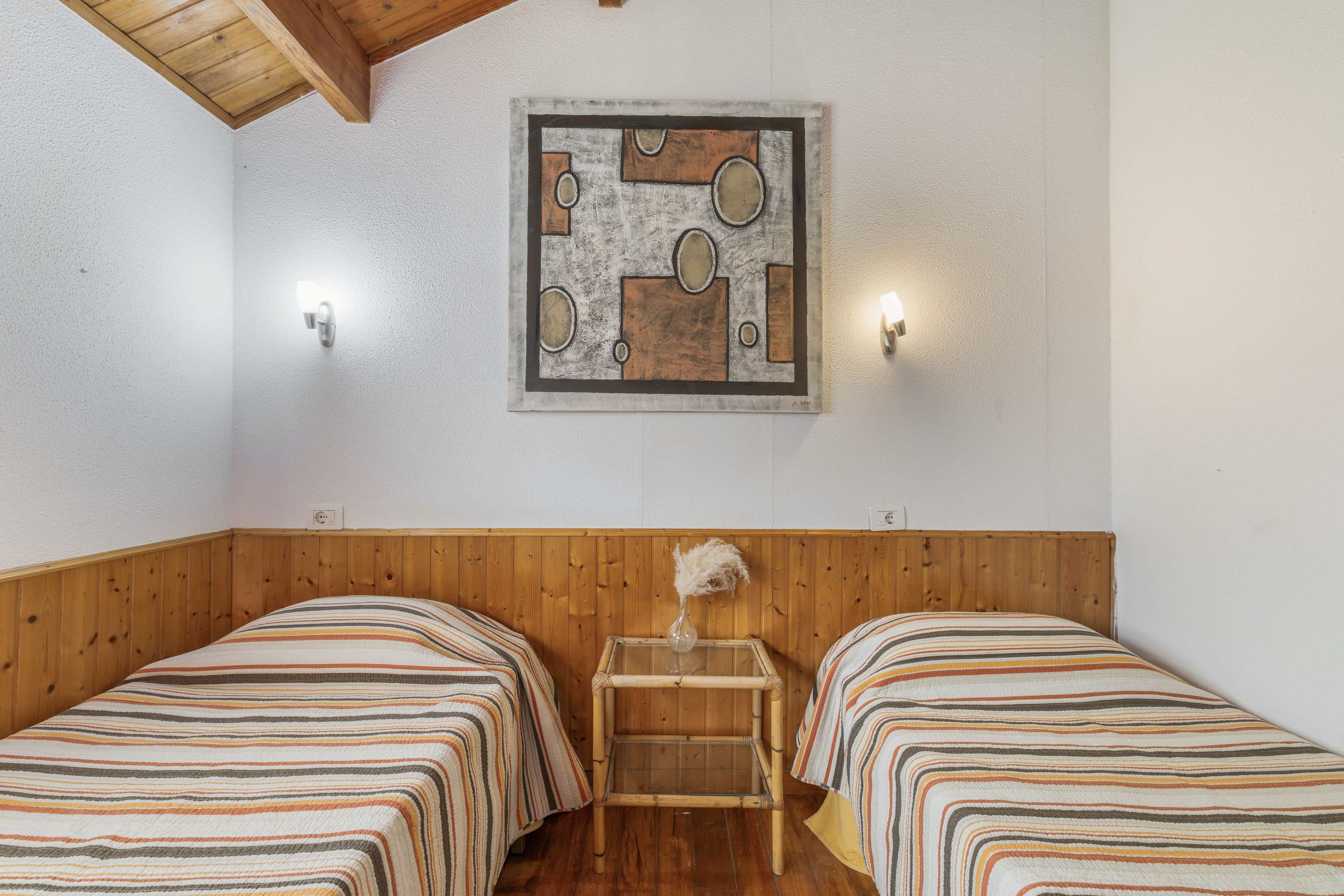 Een kamer met twee bedden, houten lambrisering, een kunstwerk aan de muur en twee wandlampen.