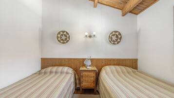 Habitación con dos camas individuales, cabecera de madera, mesita de noche con lámpara y dos luces fijadas a la pared.