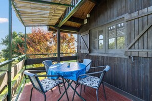 Une terrasse extérieure avec une table ronde et des chaises, une clôture en bois et une vue sur des arbres aux feuilles d’automne.