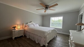 A bedroom with a bed, a nightstand with a lamp, a ceiling fan, a window, and a dresser.