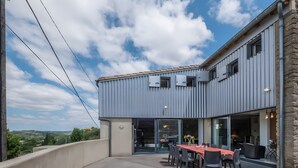 Un edificio moderno con un balcón, un comedor con mesa y sillas, y vistas al campo.