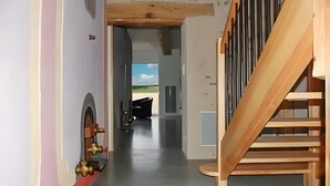 Un pasillo con vistas al exterior, una escalera de madera y una puerta con picaporte de latón.