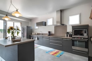 Une cuisine moderne dotée d’un îlot central, d’appareils électroménagers en acier inoxydable et de luminaires suspendus.