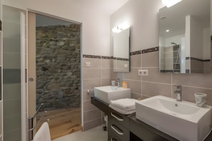 A modern bathroom with a stone wall, two sinks, a mirror, and a shower.