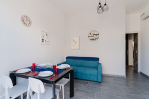 Zona pranzo con tavolo apparecchiato per quattro persone, un divano blu e orologi a parete.