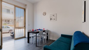 Un salon moderne avec un canapé de couleur turquoise, une table à manger avec des chaises, une porte-fenêtre coulissante donnant sur l’extérieur et une horloge murale.