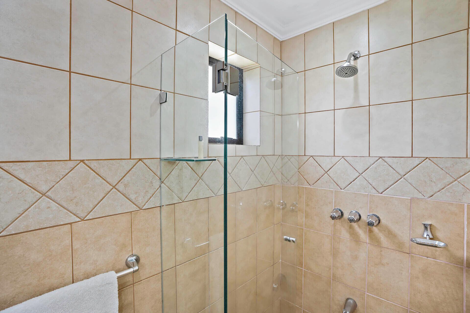 A modern bathroom with beige tiles, a glass shower enclosure, a towel rack, and a showerhead.