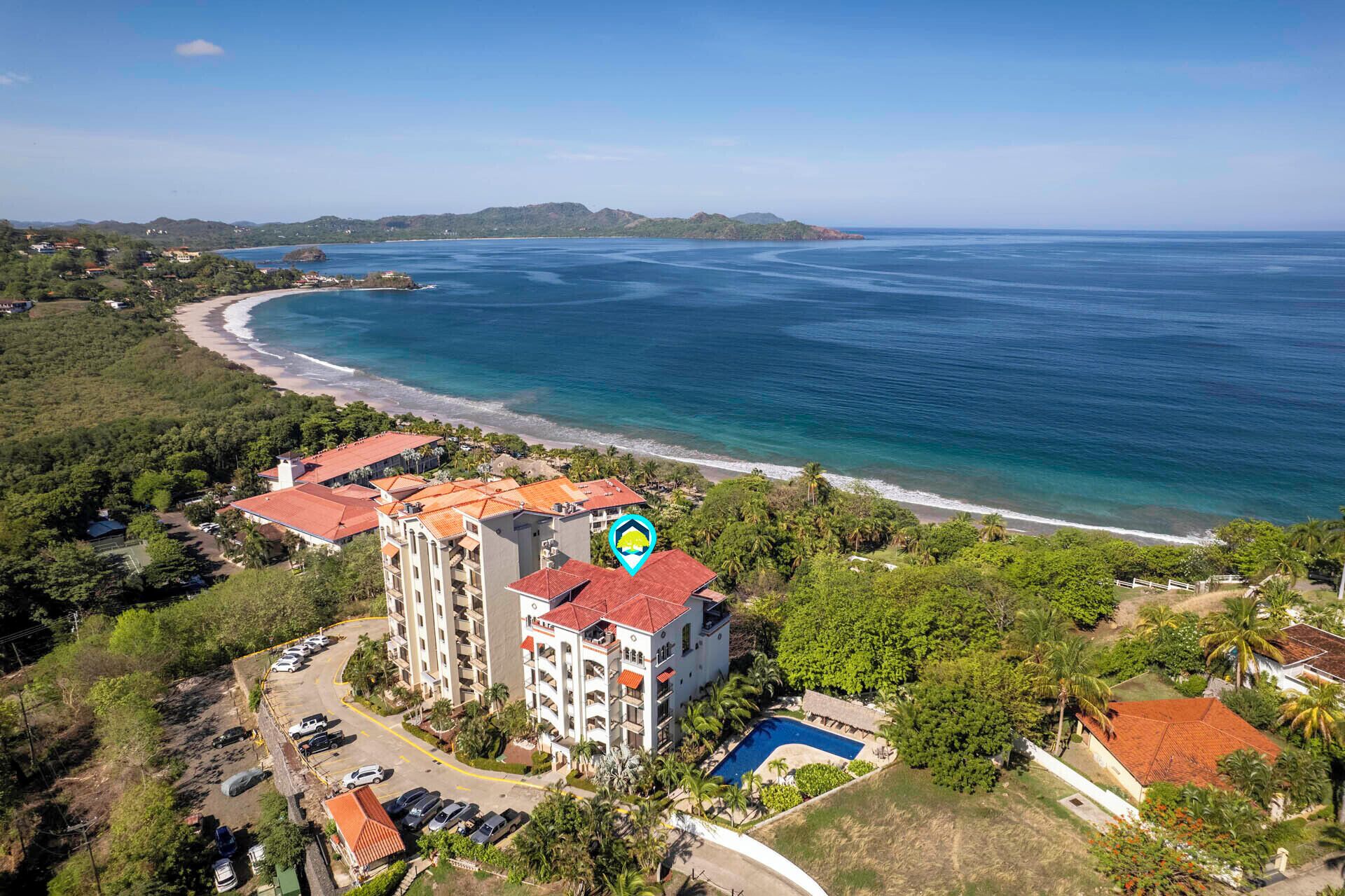 An aerial view of a coastal hotel with multiple buildings, a swimming pool, and a beach.