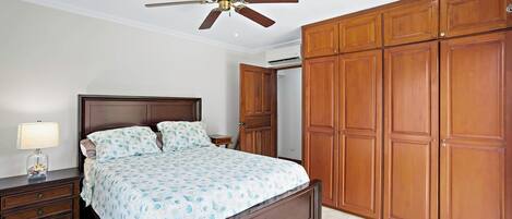 A bedroom with a bed, nightstand, lamp, wooden wardrobe, and ceiling fan.
