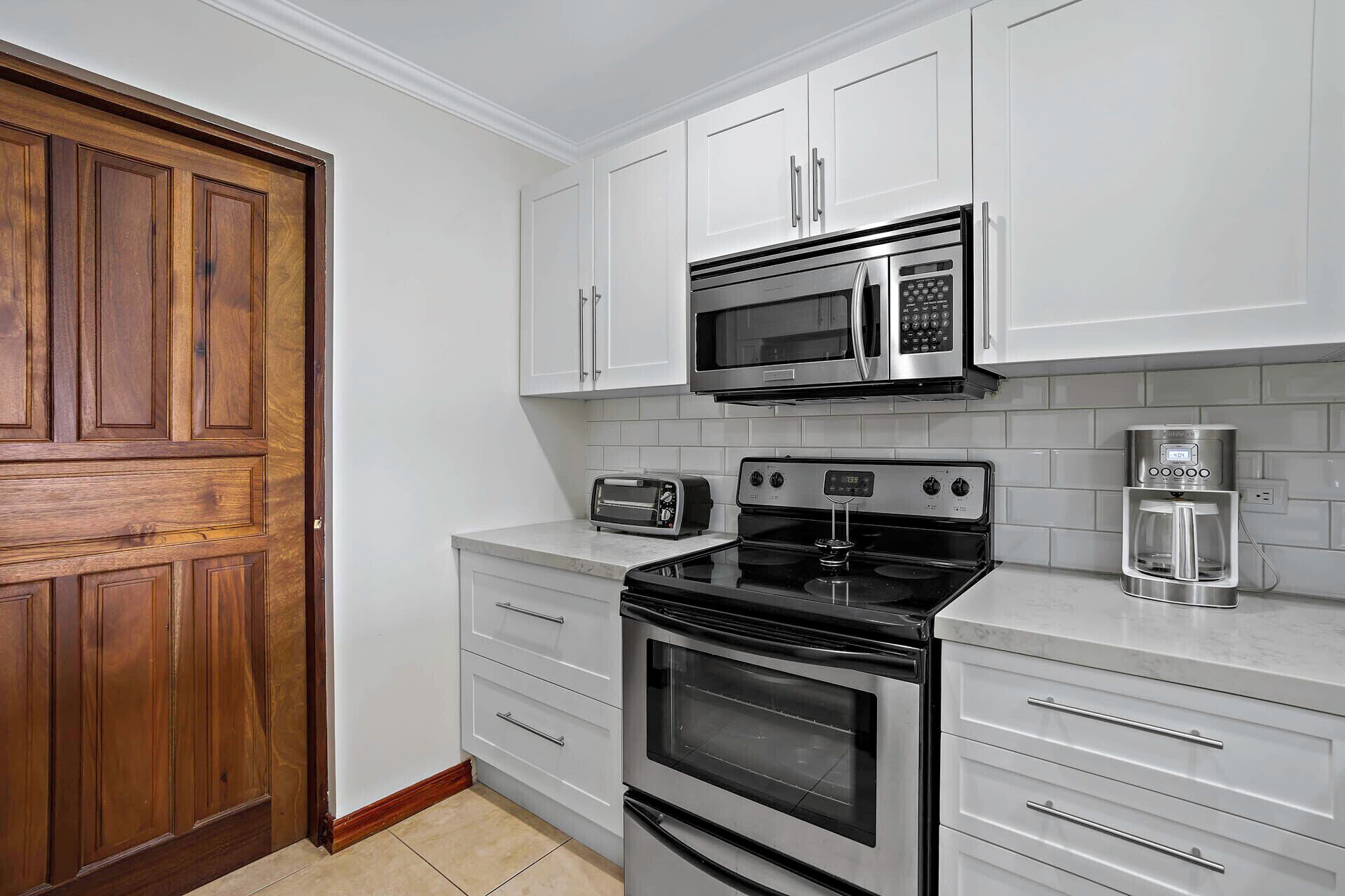 A kitchen with white cabinets, a stainless steel microwave, a toaster, a coffee maker, and an oven.