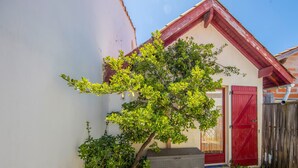 Un petit arbre se trouve devant un bâtiment dont la porte est rouge et qui est entouré d’une clôture en bois.