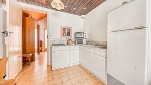 Une cuisine avec des meubles blancs, un four à micro-ondes, un réfrigérateur et un plafond en bois.