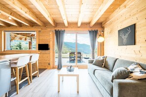 L’intérieur d’un chalet en bois comprend un coin repas, un canapé et une grande fenêtre avec des rideaux.
