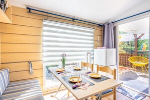 Eine moderne Küche mit Einbauofen, ein Essbereich mit Tisch für vier Personen und eine Glastür, die zu einer Terrassensitzgruppe im Freien führt.