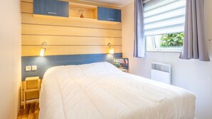 Un dormitorio con cama, almacenamiento empotrado, lámparas de noche, una ventana con cortinas y un calentador fijado a la pared.