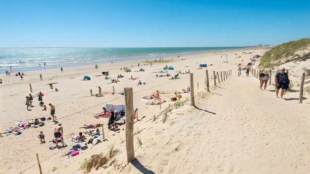 Una playa con gente tomando el sol y caminando por la orilla.