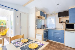 A compact kitchen with a microwave, stove, and cabinets, a dining area with a table and chairs, and a view of the outdoors.